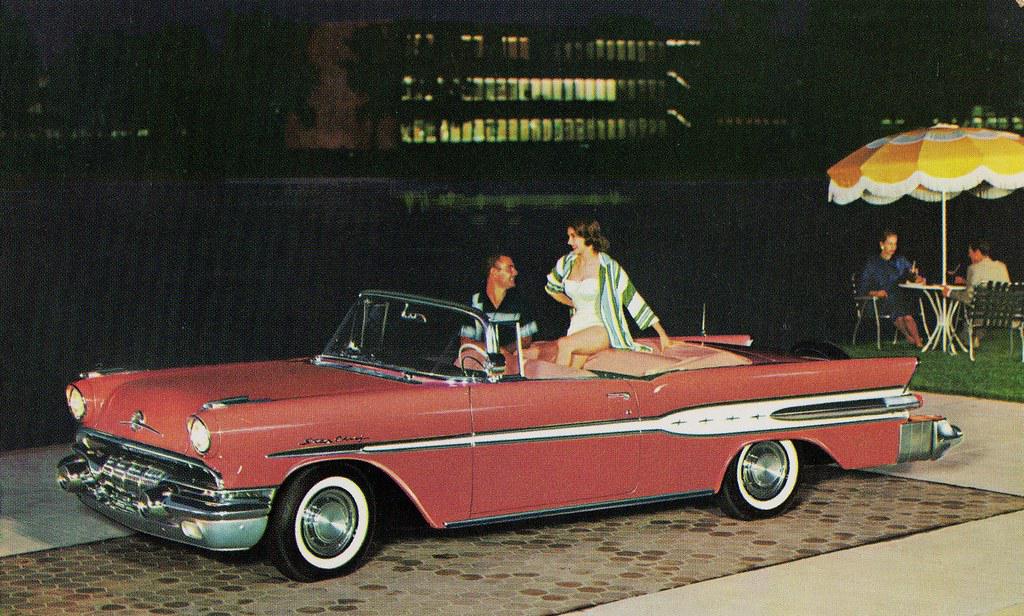 A sleek 1957 Pontiac Bonneville convertible in vibrant red, showcasing its classic V8 engine and chrome details
